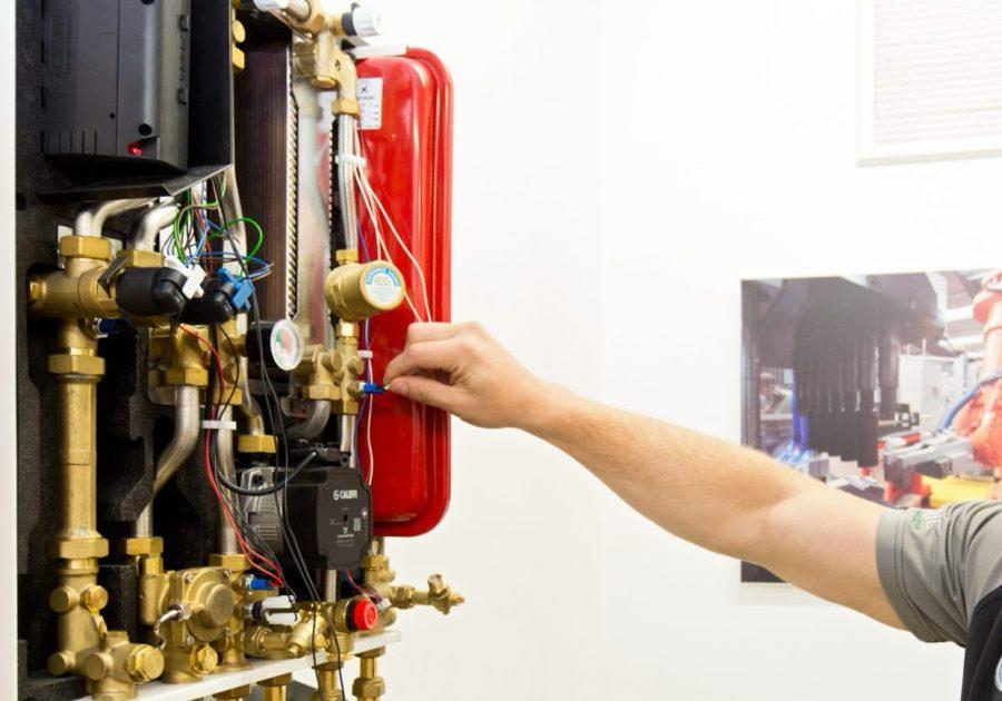 Gas engineer servicing the brass pipework, wiring and red expansion vessel inside a wall-mounted heat interface unit.