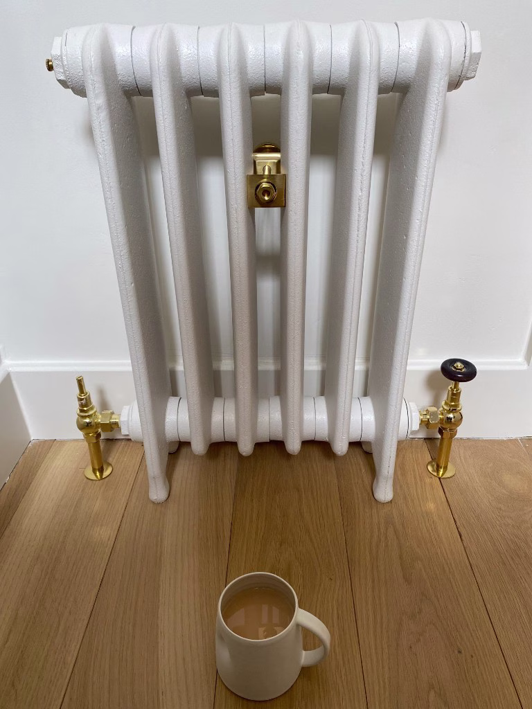 White column radiator with brass valves on a wood floor