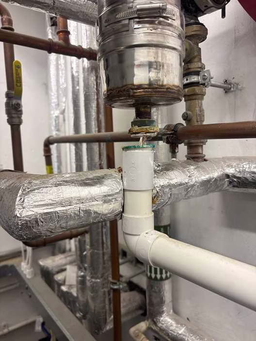 Pressure relief valve dripping into a white Saniflo macerator in a Westminster plant room