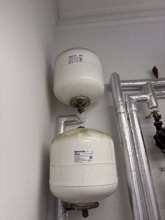 Two white wall-mounted Aquasystem expansion vessels found uncharged in a Westminster plant room